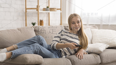 活泼的女孩躺在家里的沙发上看电视