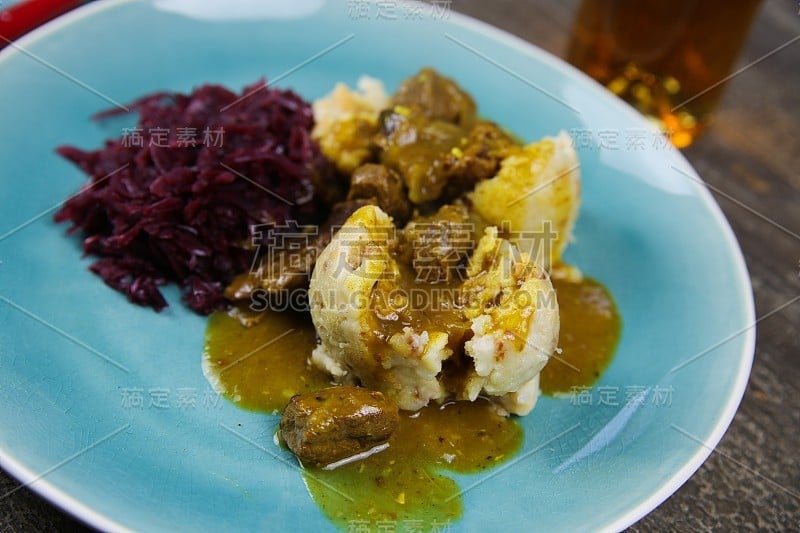 典型的德国丰盛的食物:特写的饺子与棕色酱汁，红卷心菜，牛肉炖牛肉在蓝色的中国菜