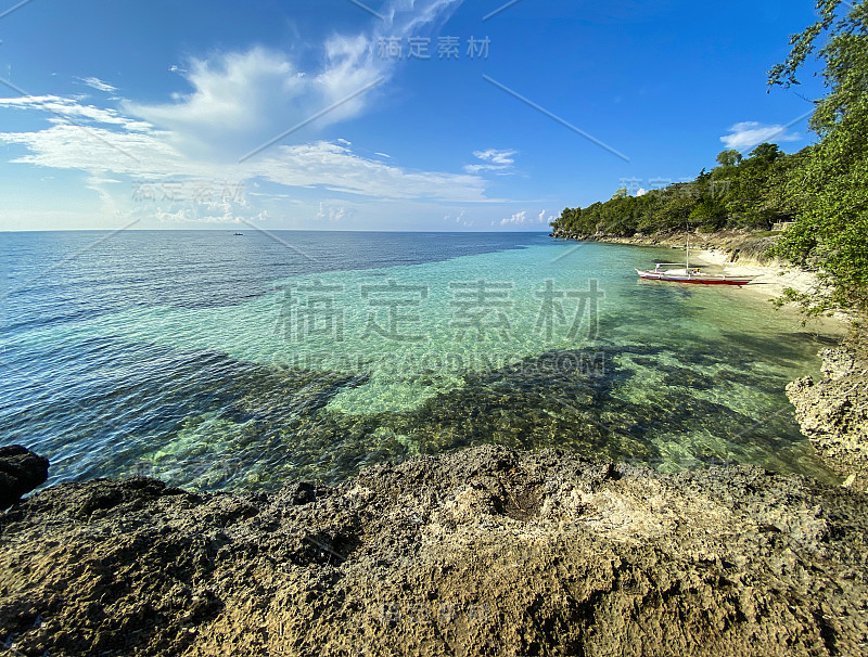 令人惊叹的美丽风景，岩石海岸背景，透明的绿松石海和蓝天白云。一艘靠近沙滩岸边的船，靠近树林