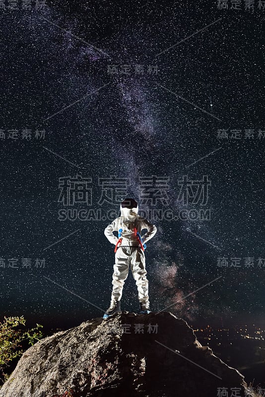 在星空下，宇航员站在岩石山上。