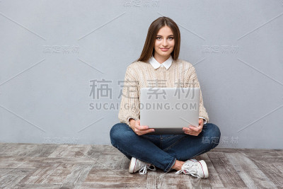 年轻自信的女人坐在木地板上使用笔记本电脑