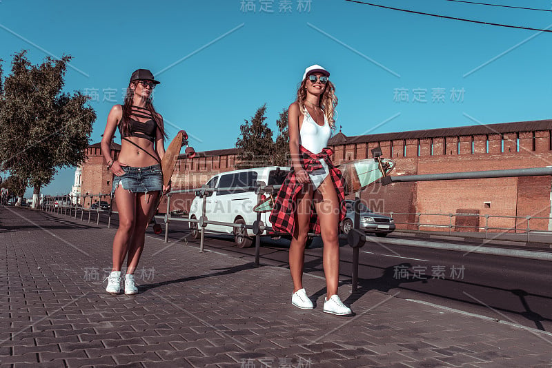 两个女孩的闺蜜漫步城市夏天，背景是公路车楼，休闲服装，手握长板滑板。周末漫步，情绪放松舒心愉悦。文本