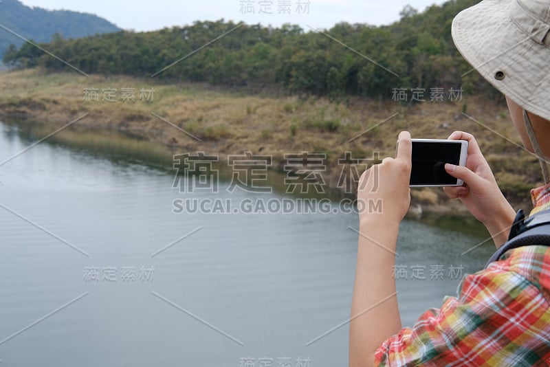 背包旅行者在森林和湖泊旅行。旅游背包客用智能手机拍照。生活方式，暑假概念