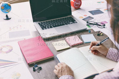 商务女性工作在办公桌上的笔记本电脑，邮寄它，笔记本和配件在办公桌上。