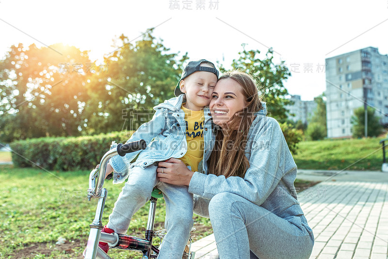 幸福年轻的家庭，女人妈妈带着孩子男孩，骑自行车，学习帮助父母支持，抚养孩子，第一堂自行车课。在夏天的