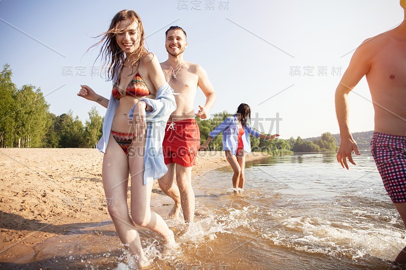 一群快乐的朋友跑到水-活跃的人在海滩上享受假期