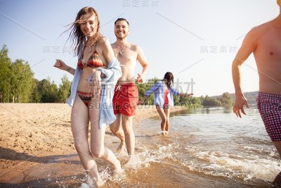一群快乐的朋友跑到水-活跃的人在海滩上享受假期