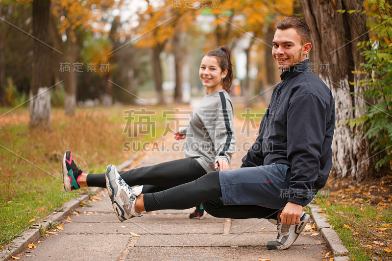 一对幸福的年轻夫妇蹲在街道上，用播种的手保持着平衡。在秋天的公园。