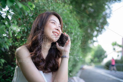 迷人的亚洲美女坐在绿色草地上谈论智能手机