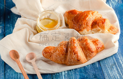 脆脆的牛角面包和一罐蜂蜜在轻织物上，美味的蜂蜜糕点