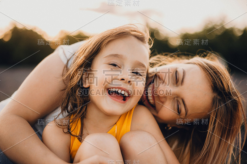 迷人的母亲和她的女儿玩在阳光下拥抱她在田野