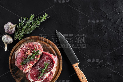 牛柳片，用刀切肉，调味料-迷迭香，胡椒，盐，大蒜。旧木板上的石头黑色桌子