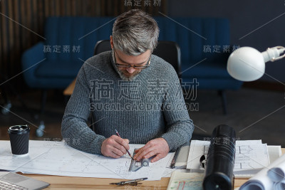 室内设计师在办公室工作与蓝图。工程师检查建筑平面图，为建筑工程画草图。英俊的胡子男人在工作场所的肖像