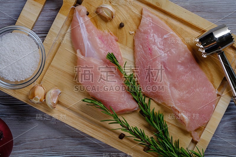 木板上放着新鲜的生鸡胸肉，木桌上放着香料和香草