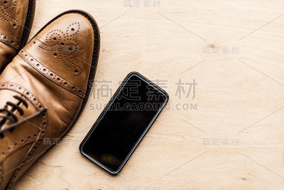 智能手机和棕色皮鞋在木质表面上