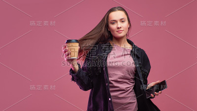 年轻的学生，手里拿着一个硬纸板咖啡杯和一部智能手机。