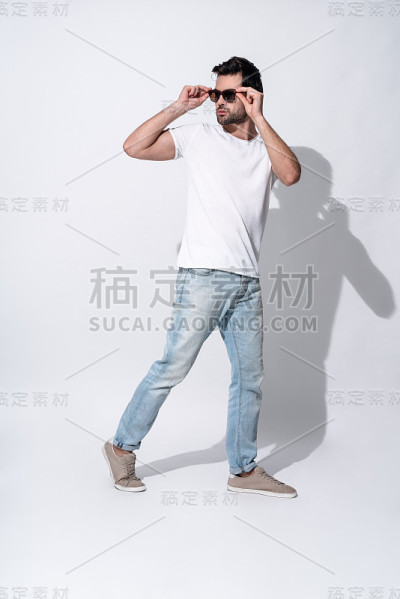 全长英俊的年轻男子在眼镜和休闲装看远，而站在灰色背景