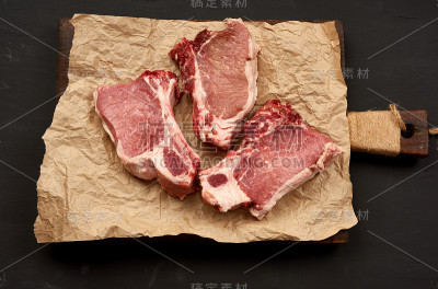 三片生的多汁的猪肉排上，食物放在棕色的羊皮纸上