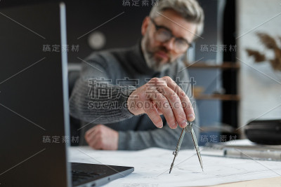 室内设计师在办公室工作与蓝图。工程师检查建筑平面图，为建筑工程画草图。英俊的胡子男人在工作场所的肖像
