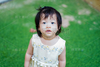 近距离观察可爱的亚洲小女孩在幼儿园操场上的绿色后院花园背景。宝宝是好奇和环顾四周，孩子教育和发展学校