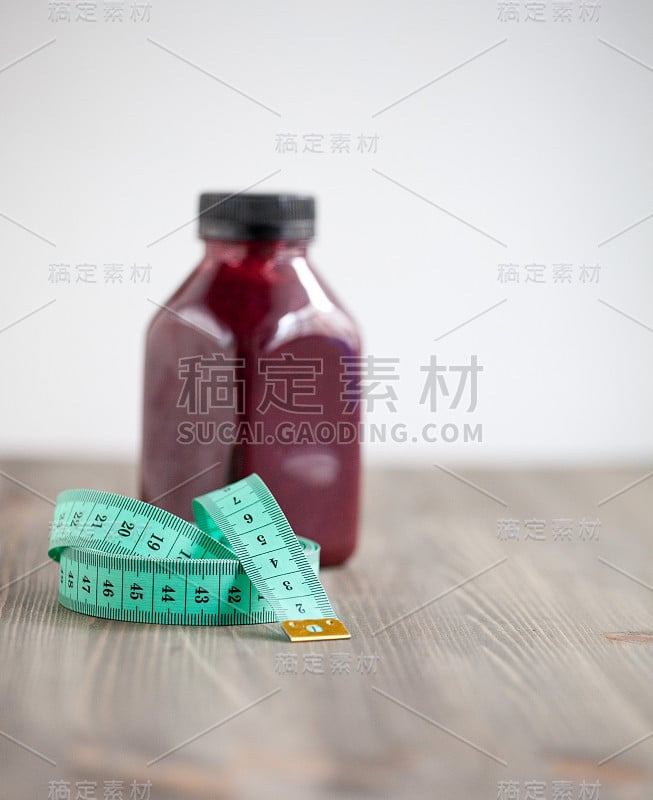 健康与健身理念。部分解开的裁缝卷尺(卷尺)与黑醋栗冰沙瓶的背景。减肥的象征