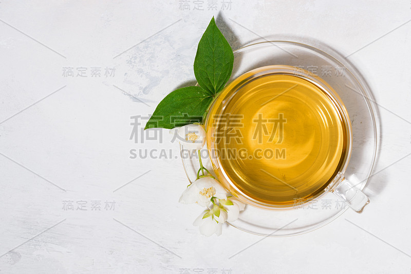 玻璃杯与绿茶在一个白色的背景和一枝茉莉花，俯视图