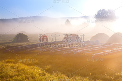 在阳光明媚、雾气蒙蒙的早晨，游客在野外露营