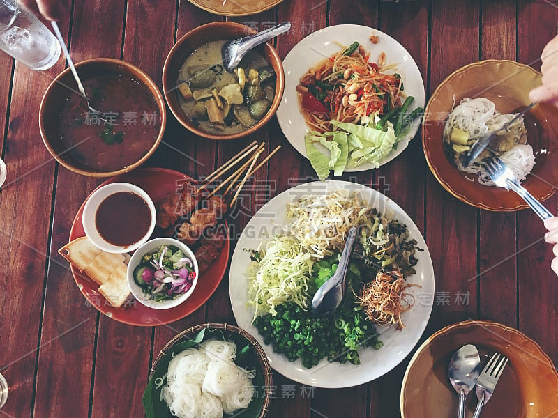 桌上摆着美味的亚洲食物。麻辣猪肉粉，沙爹猪肉，烤猪肉配花生酱或酸甜酱配蔬菜。前视图。的语气