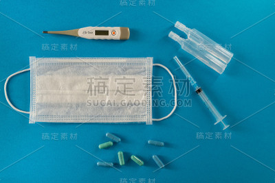 医用口罩，药片，温度计，注射器，蓝色背景上的小瓶。冠状病毒，流感概念