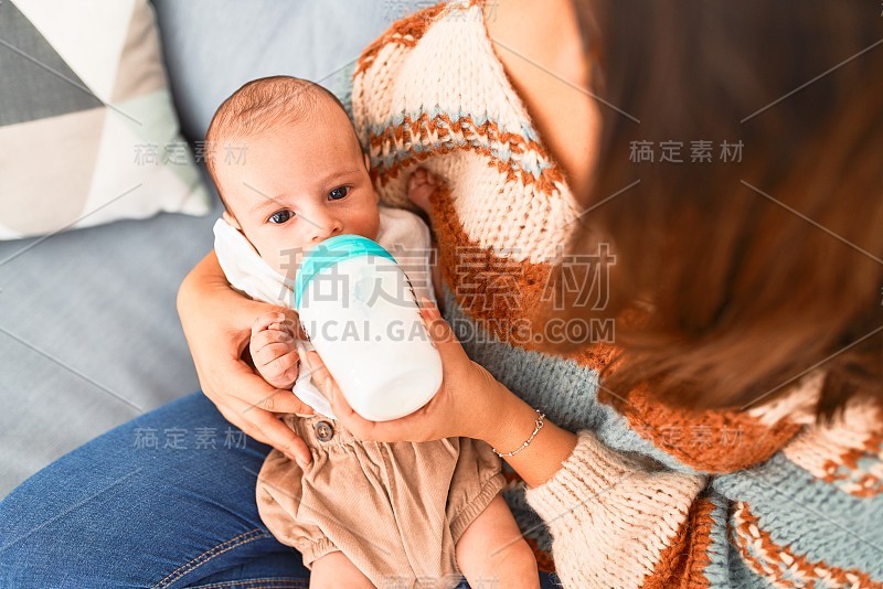 年轻漂亮的女人和她的孩子躺在家里的沙发上。新生儿和母亲放松和休息，舒适地使用奶瓶喝牛奶