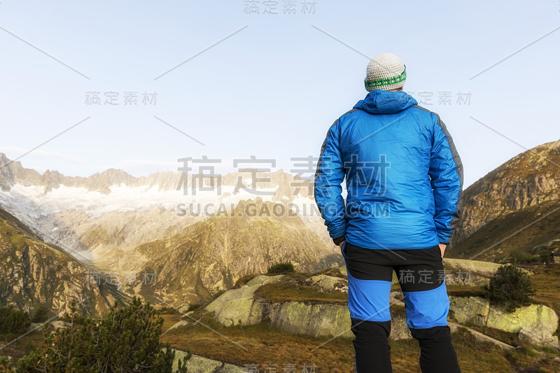 一位登山运动员在黎明时分站在瑞士阿尔卑斯山脉雄伟的山景前