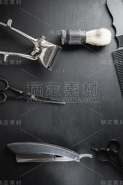在布满灰尘的黑色表面上是旧的理发工具。老式手工理发器、梳子、剃须刀、剃须刷、剃须刷、美容剪刀。黑色的