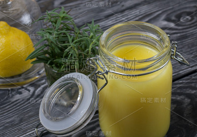 玻璃罐里的柠檬汁。旁边是半个柠檬装在一个玻璃盖的容器里。一杯迷迭香。以拉丝板为背景。