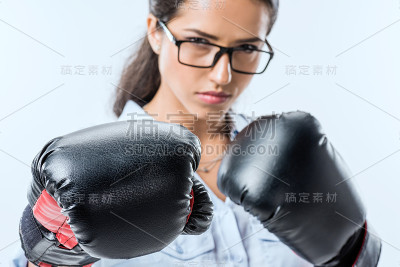 严肃的女商人的肖像在拳击手套看孤立在蓝色的相机