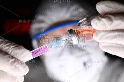 医生穿着防护服，戴着手套和口罩给注射器注水