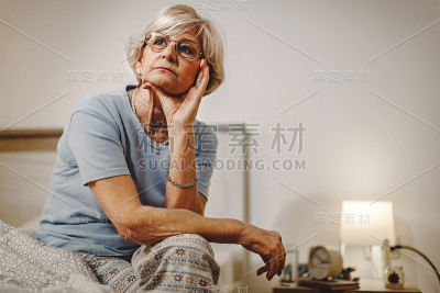 沉思的成熟女人坐在床上思考着一些事情。