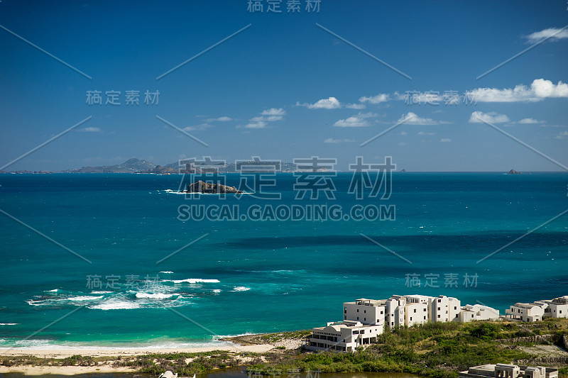 在蔚蓝的海面上的小石岛，前景是海滩和房子