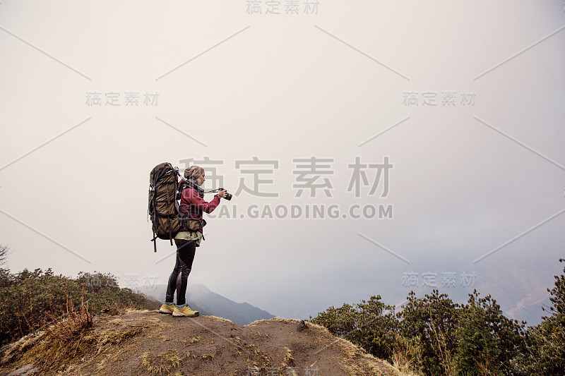 女旅行者摄影师与大背包停留在山顶的丛林森林。在尼泊尔山区徒步旅行，拍照和欣赏风景