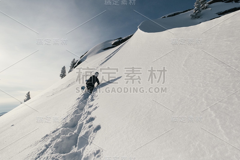 在冬季的高山中，手持滑板在深雪坡上自由行走的滑雪者。白雪覆盖的悬崖和树木