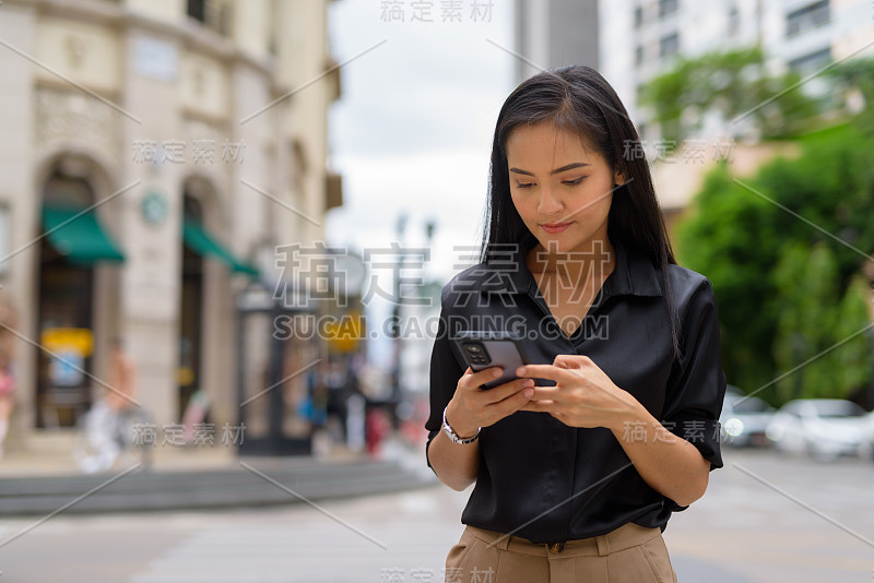 亚洲女商人在城市街道上使用手机，同时发短信