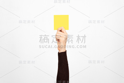 一个商人的手举着一张黄牌在空中，白色的背景。权威的概念。