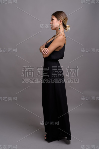 摄影室拍摄的年轻亚洲女性穿着正式的黑色连衣裙，背景是灰色