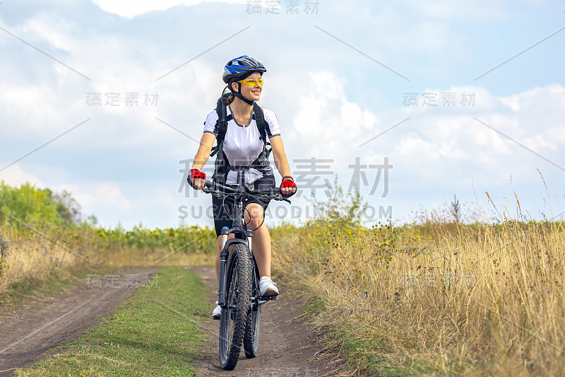 骑自行车的漂亮女孩骑着自行车在田野上。健康的生活方式和运动。业余爱好