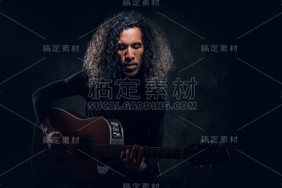 男子一边给摄影师摆姿势，一边弹吉他
