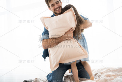 快乐的爸爸和女儿早上在床上玩枕头大战