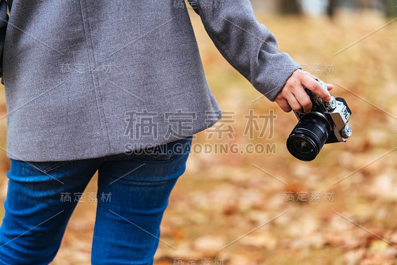 近距离拍摄女性游客一手拿着相机站在秋天棕色的落叶公共自然公园公园旅游的概念