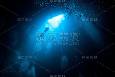 潜水员从下面带着气泡靠近蓝色明亮的坑入口