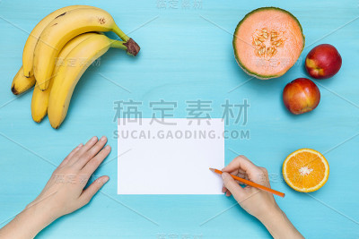 桌面上女性用手在白纸上用水果写字的场景