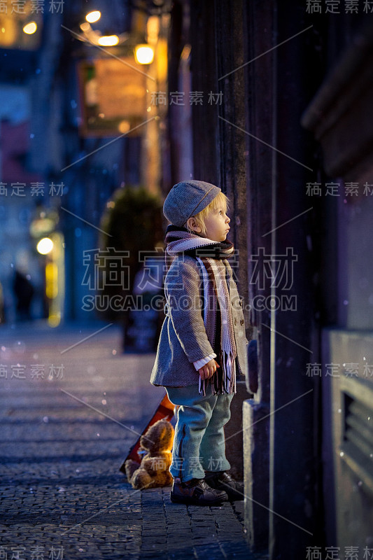 可爱的蹒跚学步的男孩，晚上在城里弹吉他，玩玩具熊