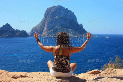 白种女孩放松做佛教冥想在悬崖前的Es Vedra岛在西班牙的海边在夏天Cala dhort